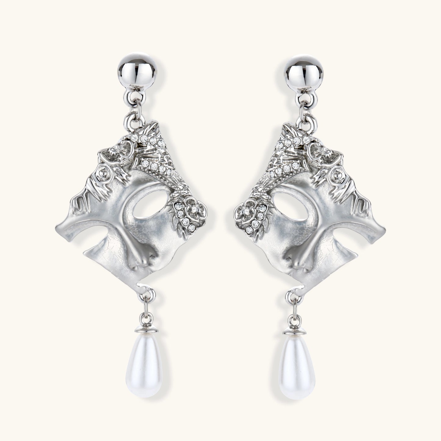 Ornate silver-toned theatrical mask earrings with crystal details and pearl drops on white background.