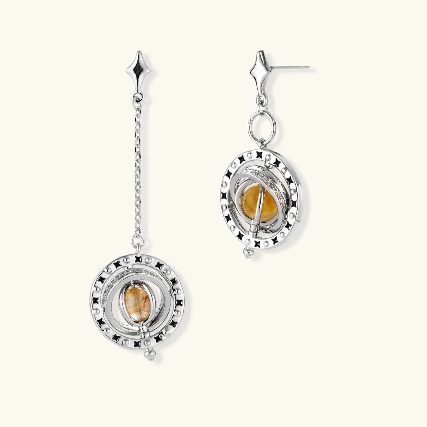 Orbital asymmetric earrings with star-shaped posts, silver-toned rings with black enamel stars, and honey-gold cabochons in pavé-set orbit from Najera Studio